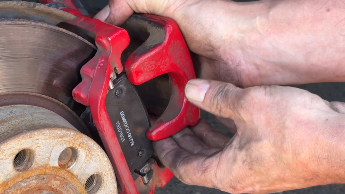 New brake pads installed, sitting flush with rotor, caliper being put into position